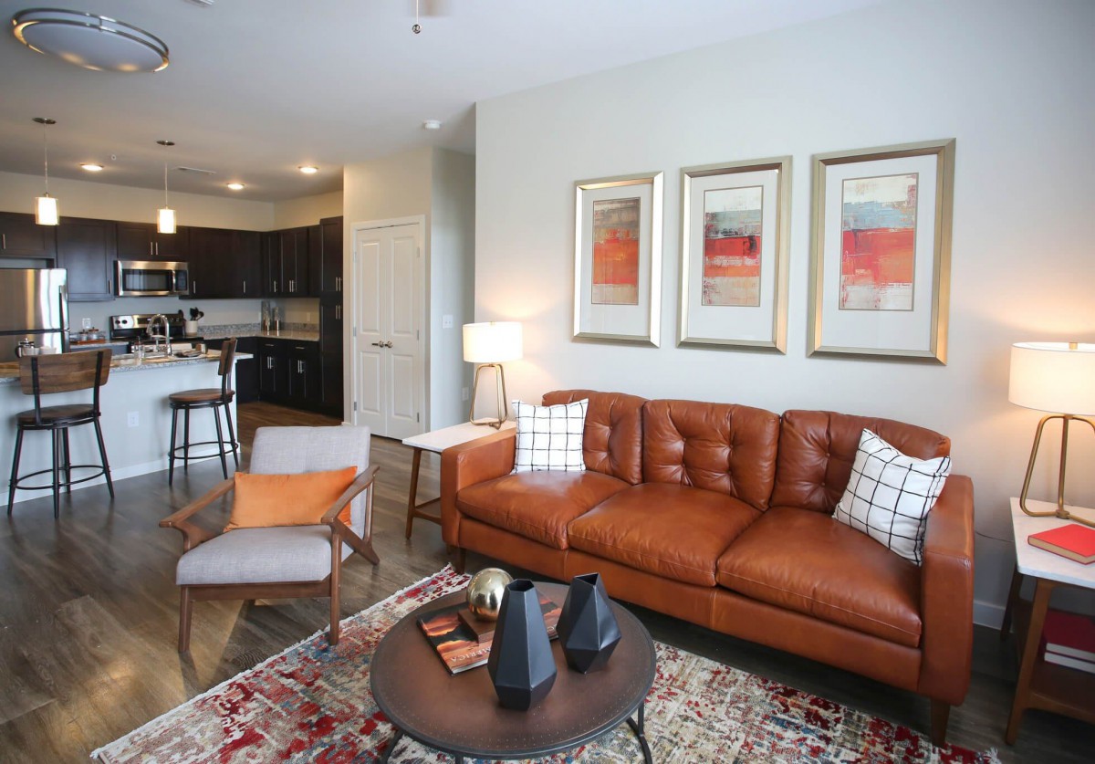 A modern living room with a brown leather sofa, abstract artwork, and an open kitchen layout.