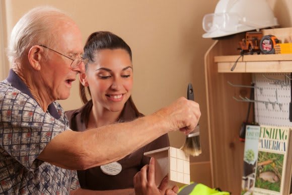 An elderly man and a young woman collaborate on a painting project.