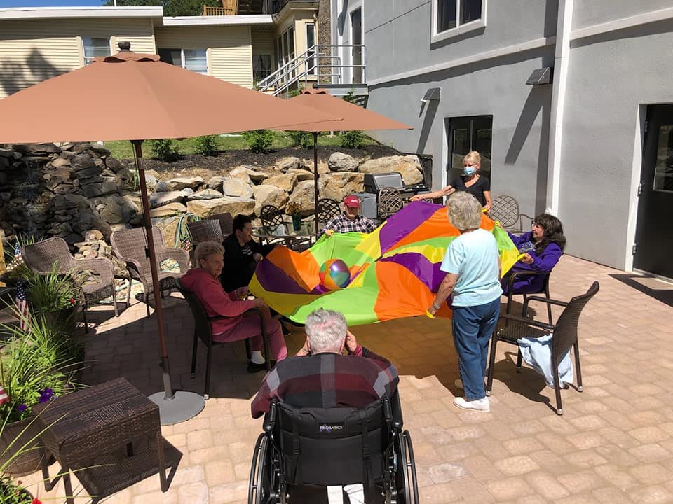 Seniors enjoying an outdoor group activity with a colorful parachute under a parasol.