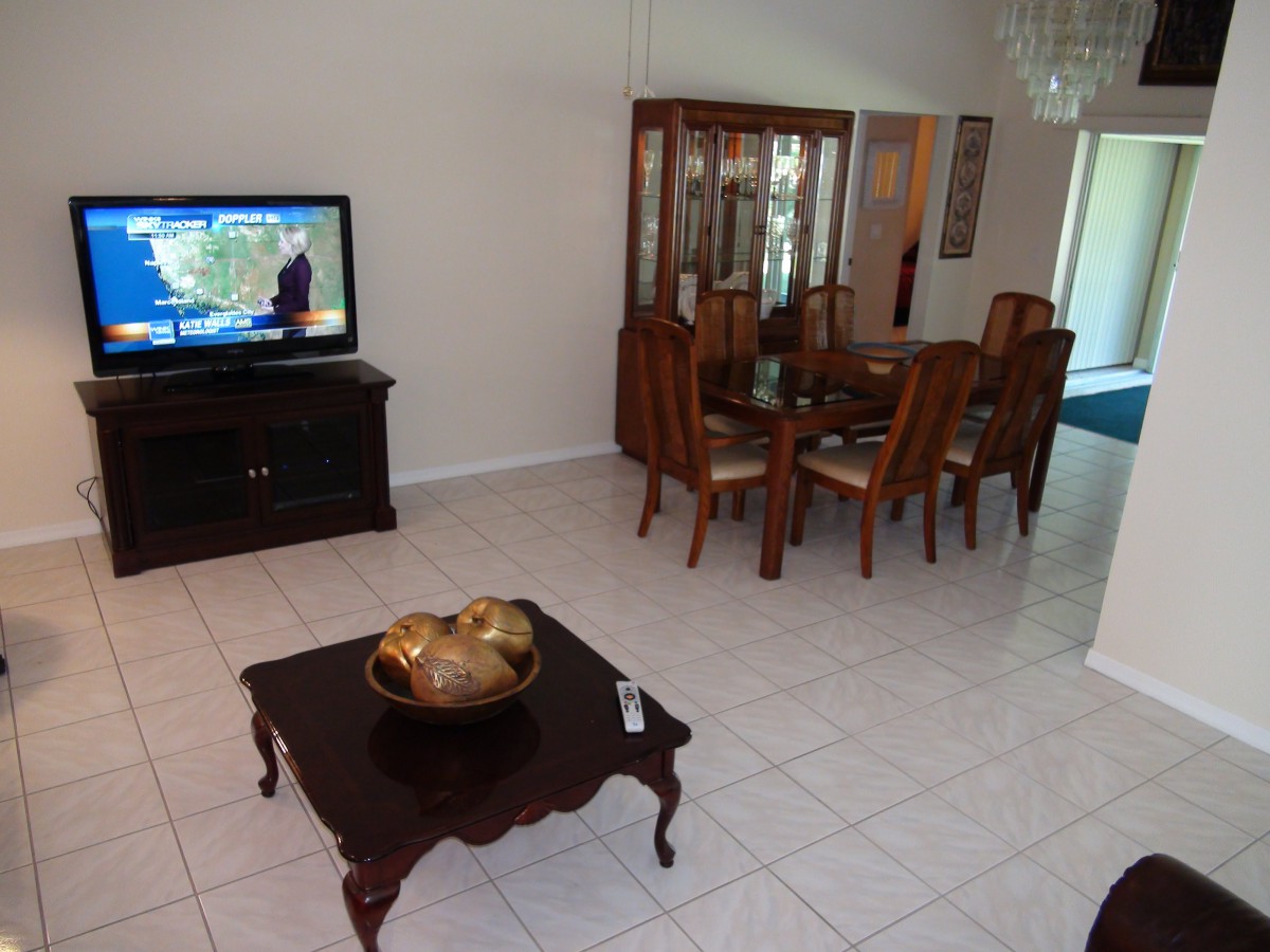 A living room with a TV and a dining table set on a tiled floor.