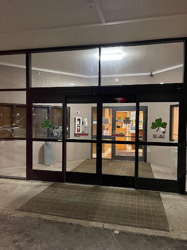 Entrance of a building at night, featuring glass doors and soft indoor lighting.