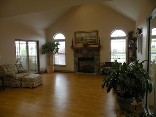 A spacious living room with a fireplace and vaulted ceiling, featuring hardwood floors and indoor plants.