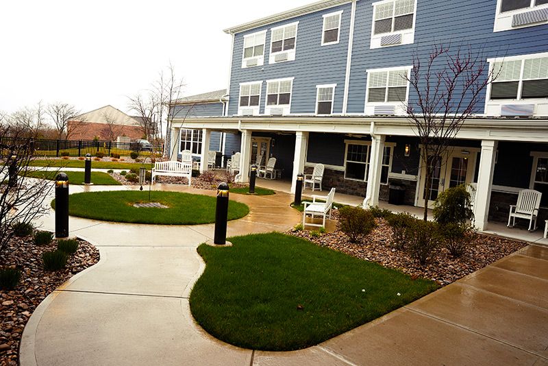 A landscaped outdoor area with a building, featuring grass, pathways, benches, and trees.