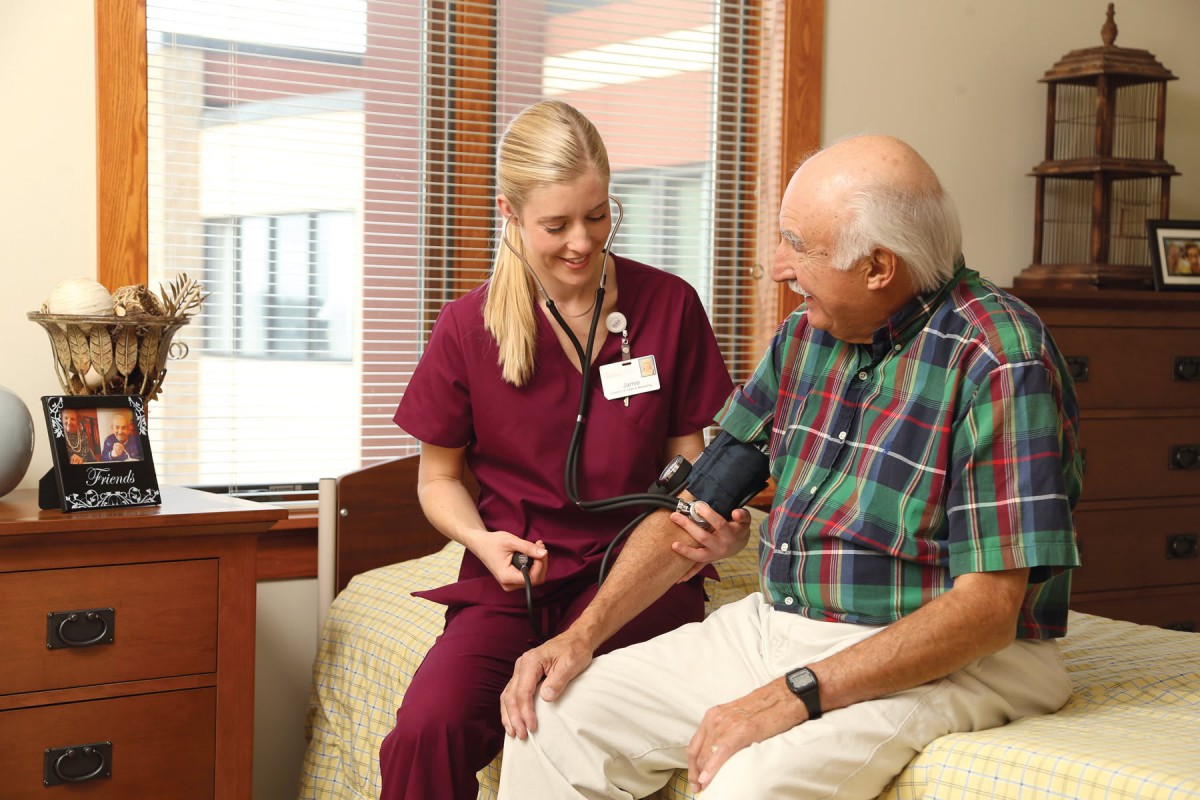 A nurse checks the blood pressure of an elderly man in a hospital room.