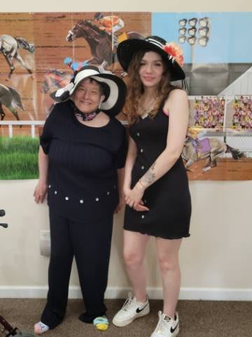 Two women wearing stylish hats and dresses pose together indoors.