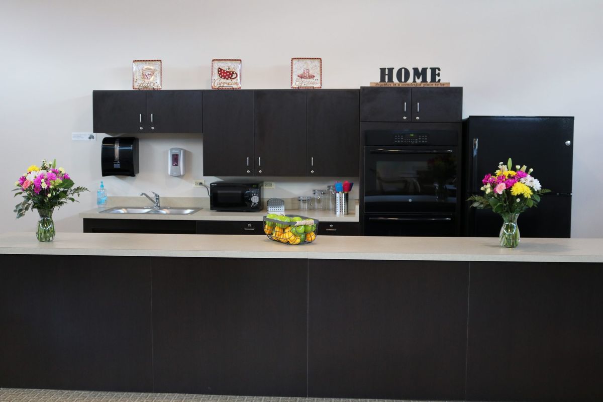 A modern kitchen with dark cabinets, a countertop featuring a fruit bowl, and decorative elements.