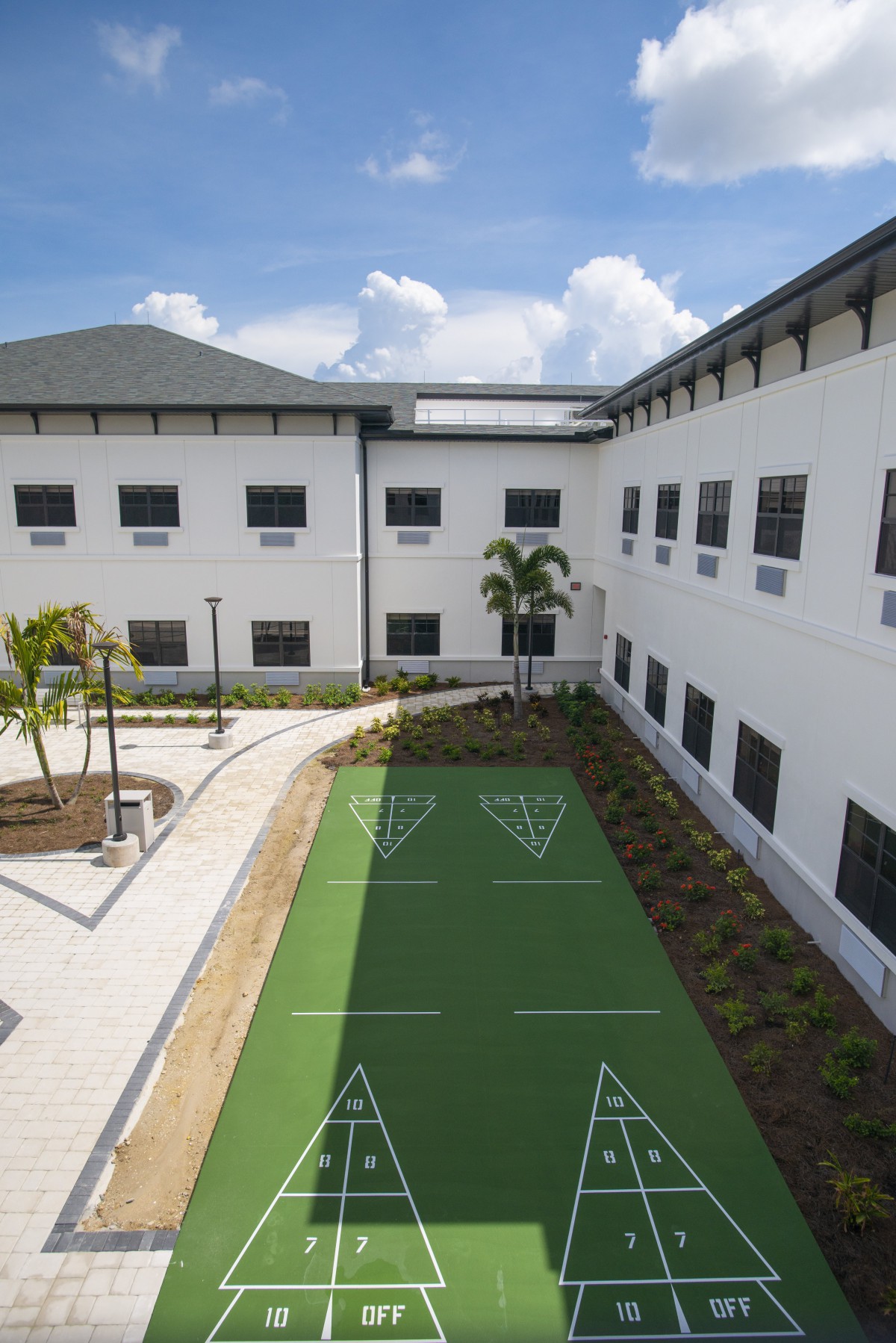 A modern building with a courtyard featuring a shuffleboard court surrounded by landscaped greenery.