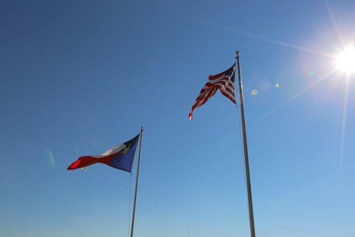The flags of the United States and the Philippines waving against a clear blue sky.
