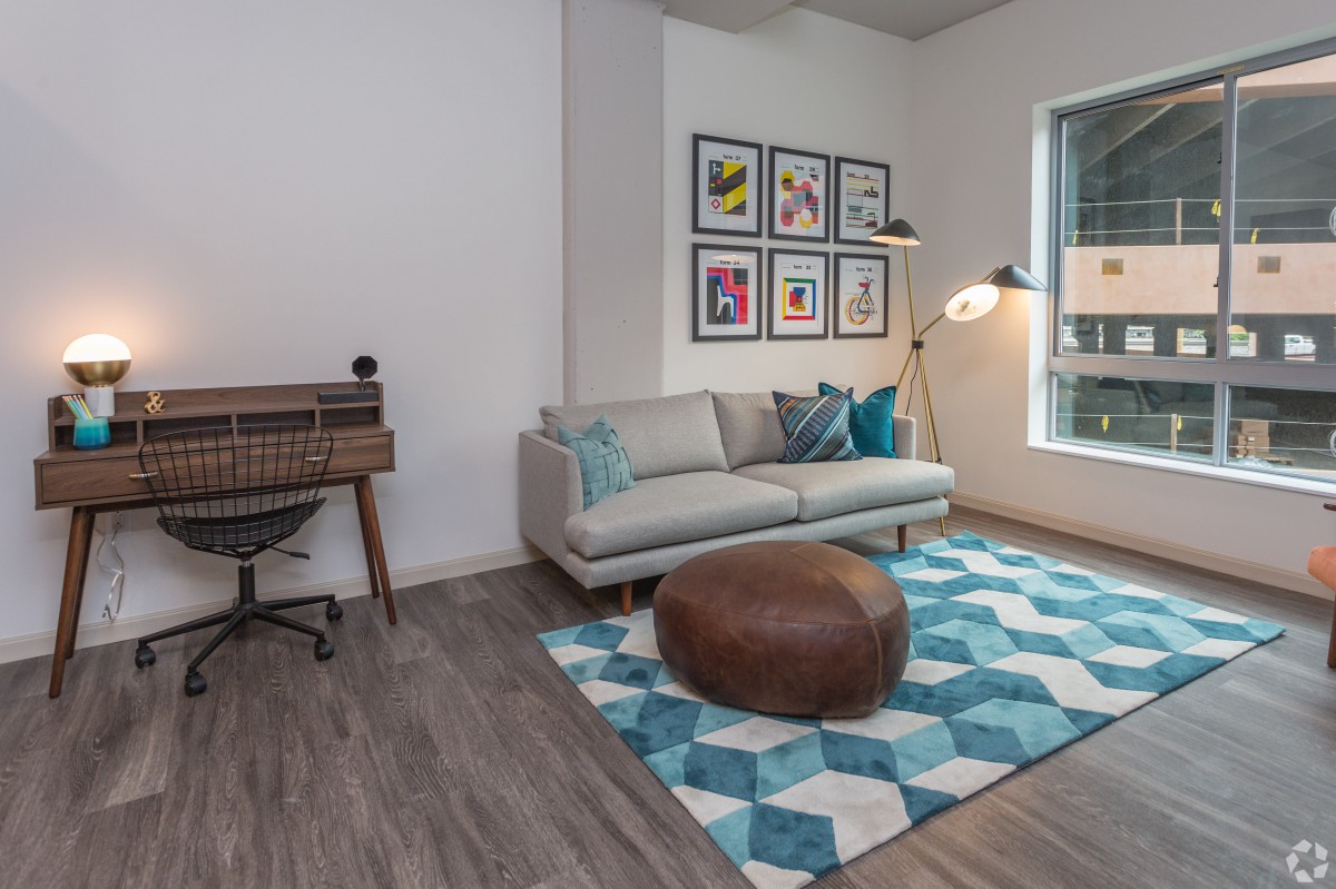 A modern living room with a stylish couch, patterned rug, and wall art, featuring a cozy workspace area.