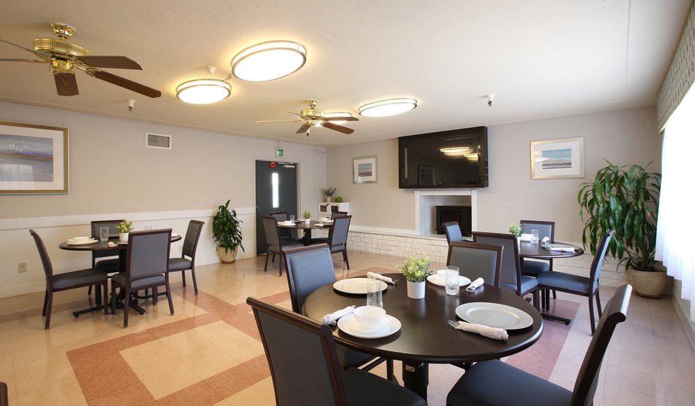 A modern dining room with neatly arranged tables and chairs, featuring contemporary lighting and a large television.