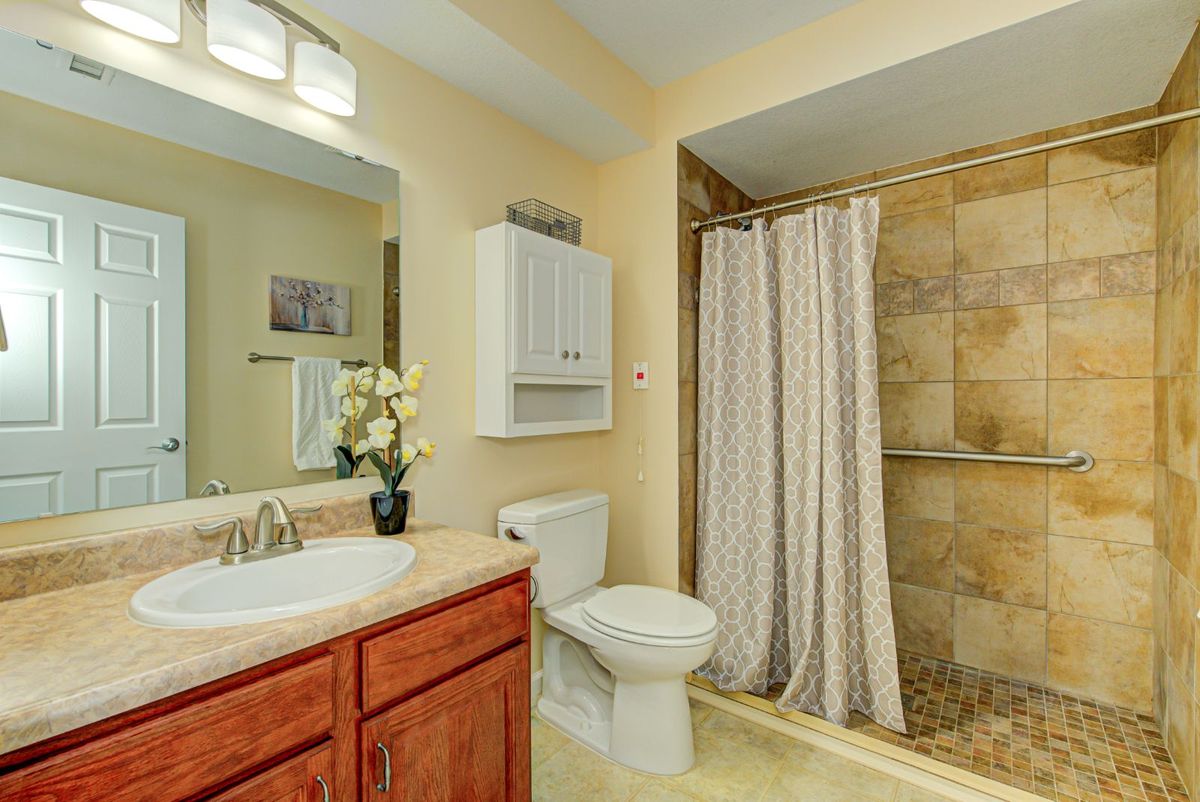 A well-lit bathroom featuring a shower with a curtain, a sink with a mirror above it, and a toilet next to a white cabinet.