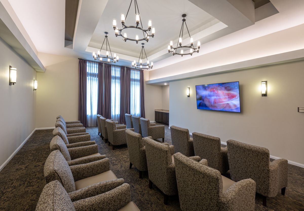 A modern conference room with comfortable seating, chandeliers, and a large television screen.
