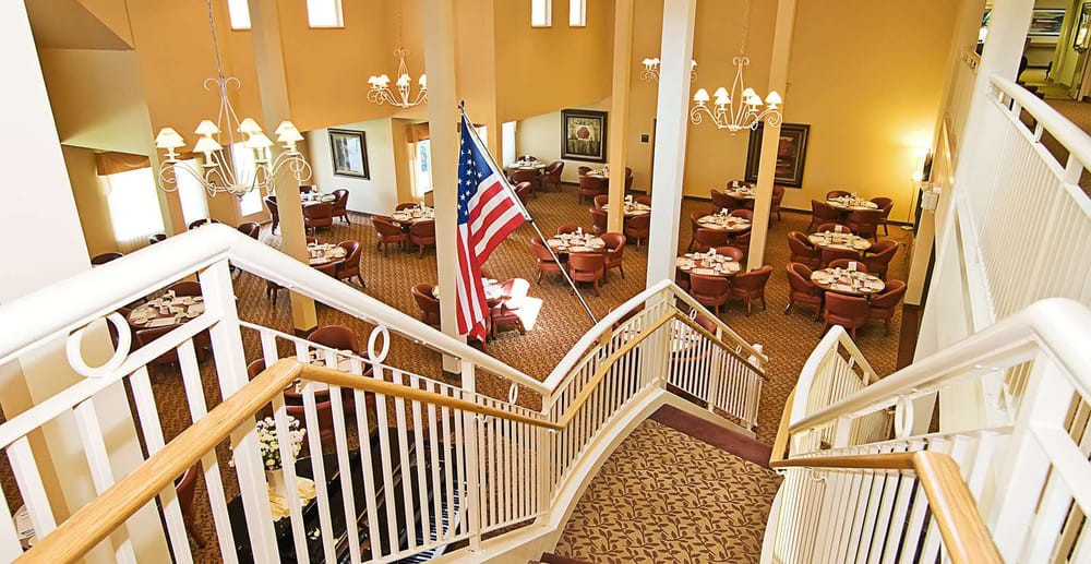 A spacious dining area with elegant chandeliers and a prominent American flag, viewed from a staircase.