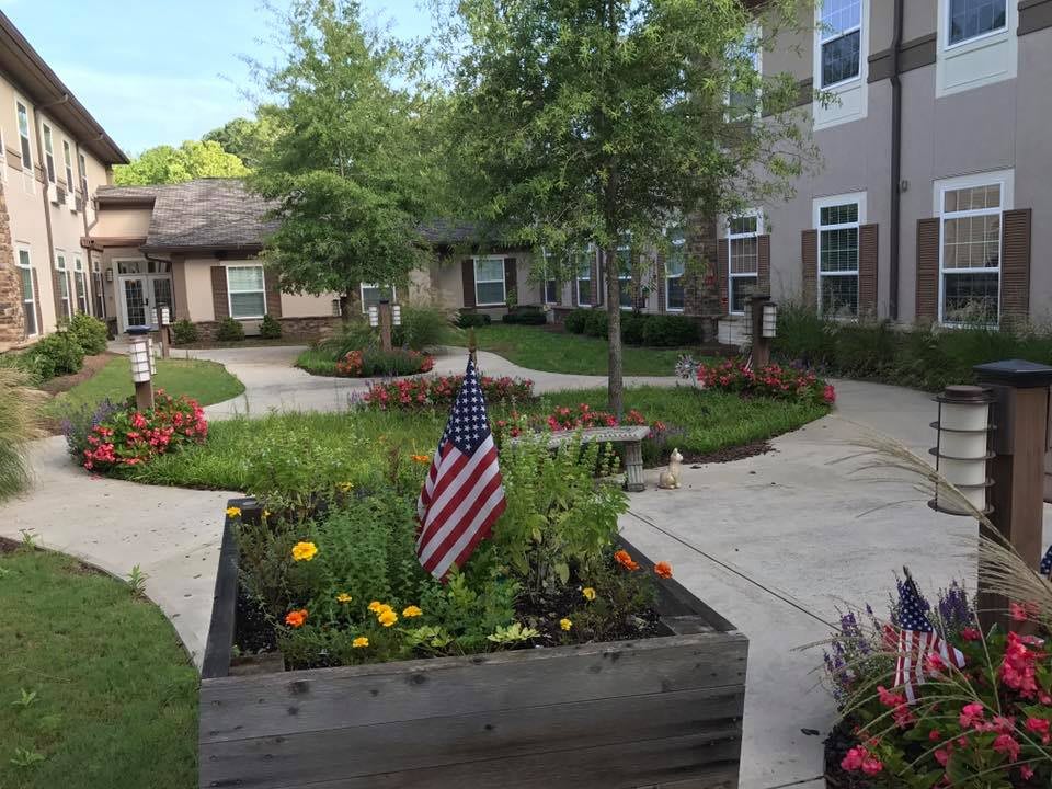 A peaceful courtyard garden with American flags, flowers, and pathways surrounded by buildings.