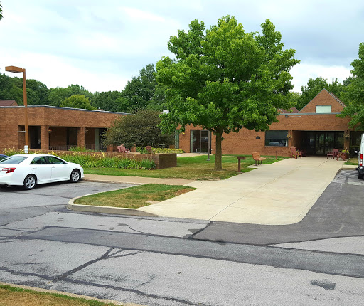 A view of a brick building surrounded by greenery and a parked white car.