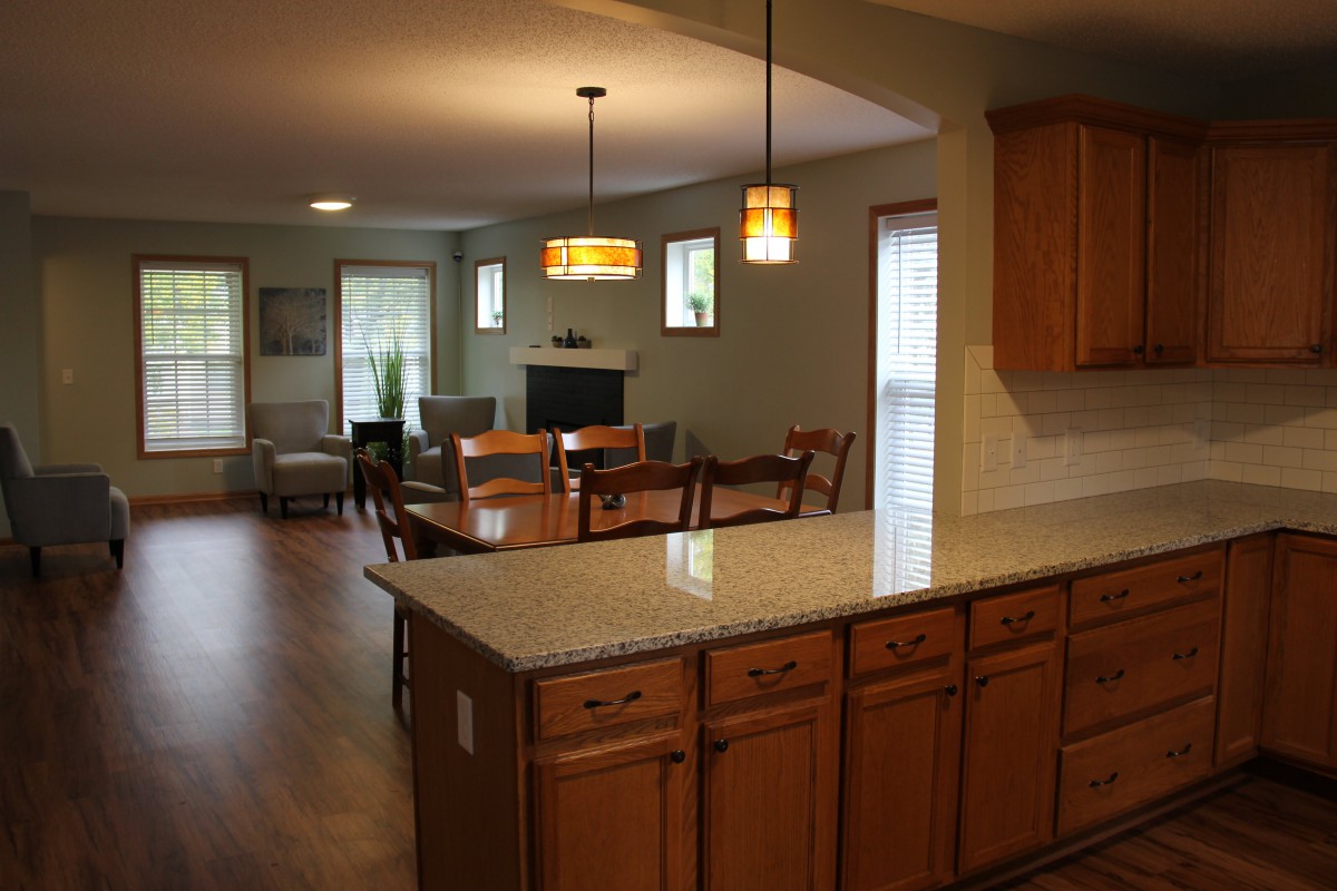 An open concept kitchen and living area with wooden cabinetry, an island, and modern lighting.