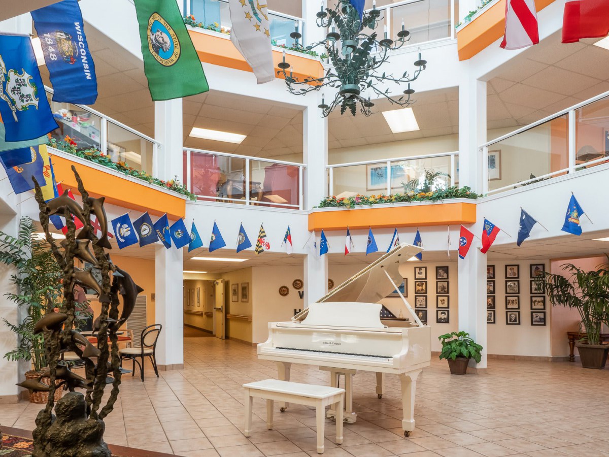 A brightly lit atrium featuring a white grand piano and surrounded by various flags hanging from the balcony.