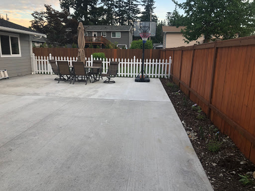 A spacious outdoor patio area featuring a basketball hoop and seating arrangements, enclosed by a wooden fence.