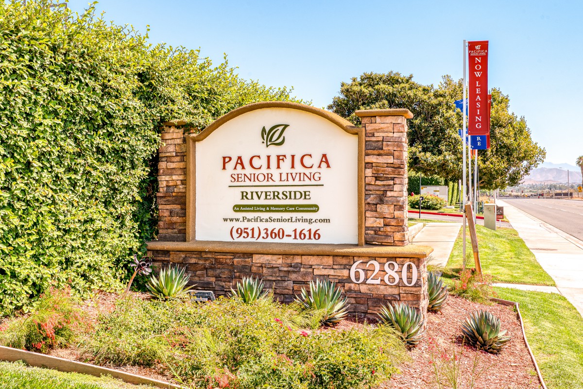 Entrance sign for Pacifica Senior Living Riverside surrounded by landscaping.