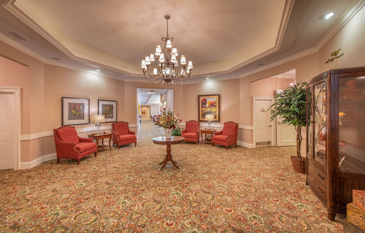 A warmly decorated lobby featuring a large chandelier, red upholstered chairs, and elegant artwork on the walls.