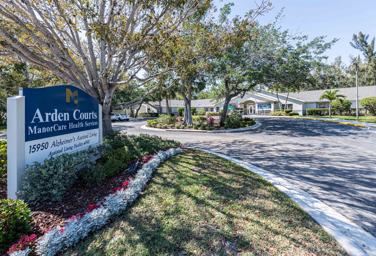 A driveway leads to a building, surrounded by trees and well-maintained landscaping.
