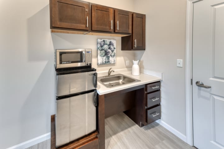 A compact kitchenette featuring a mini fridge, microwave, sink, and storage cabinets.