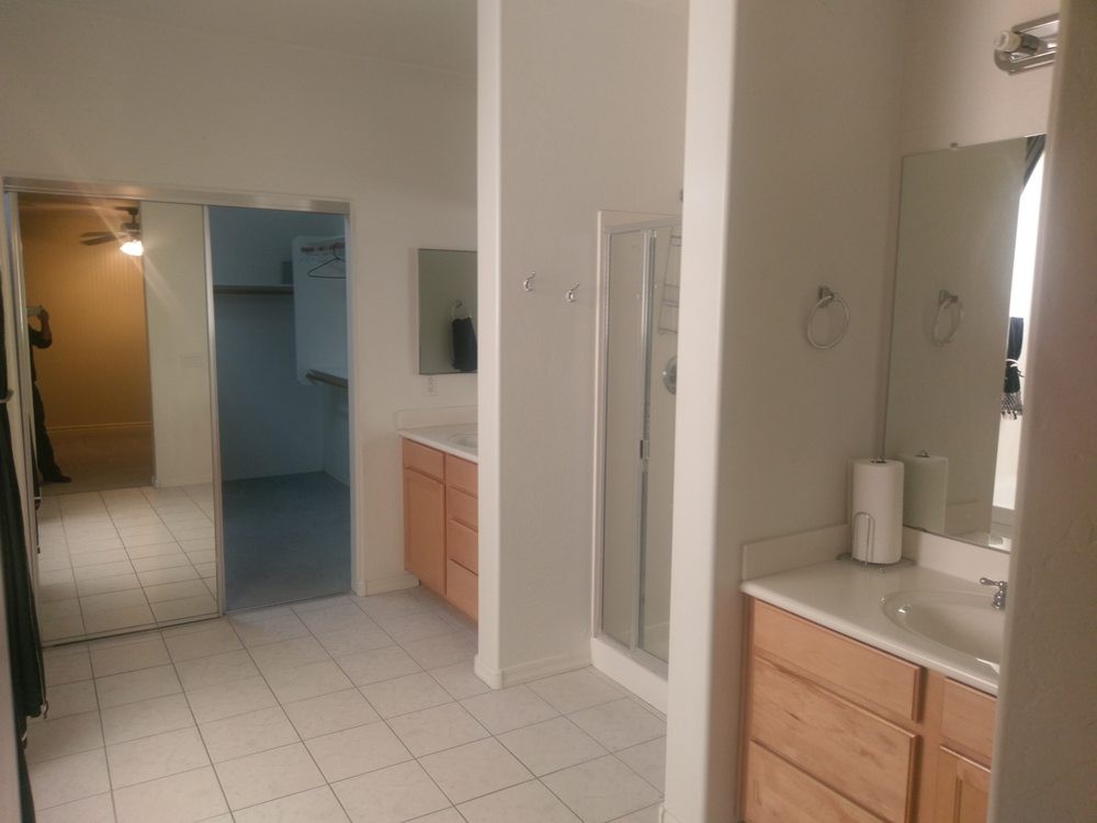 A spacious bathroom featuring two sinks, a shower, and wooden cabinets.