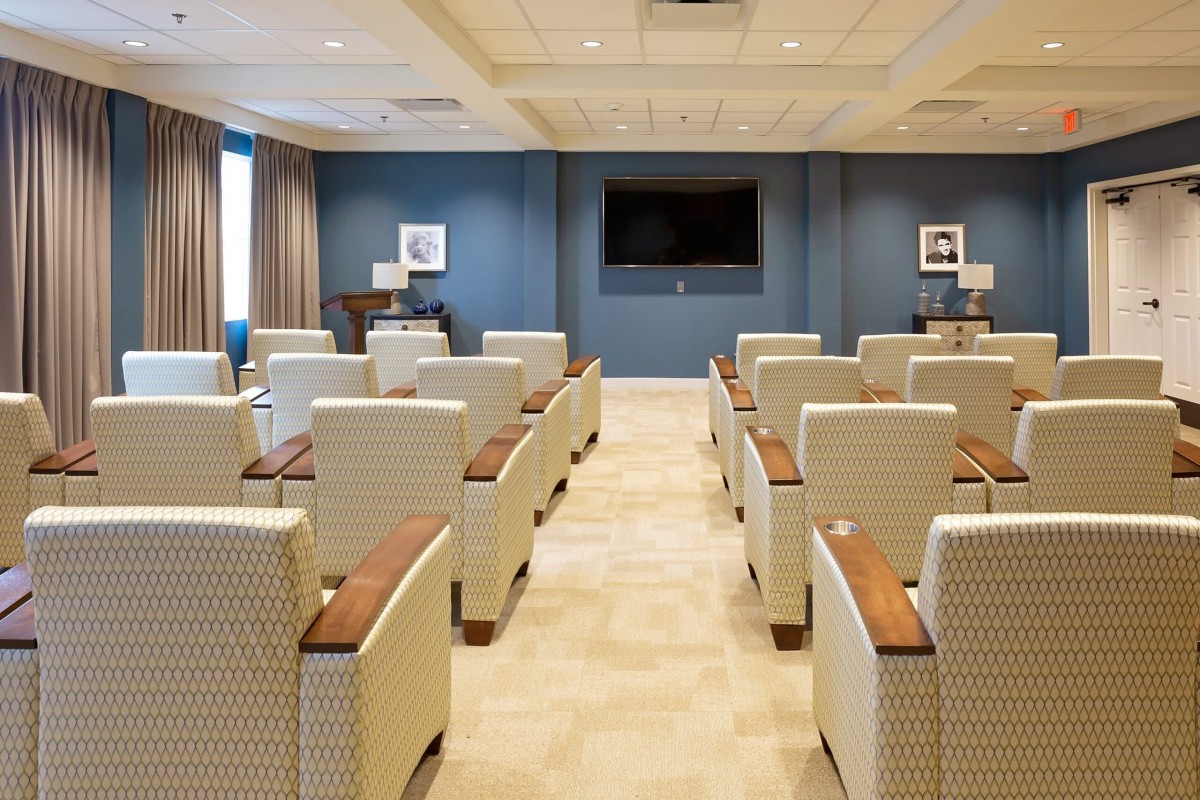 A modern conference room with rows of upholstered chairs facing a large television screen.