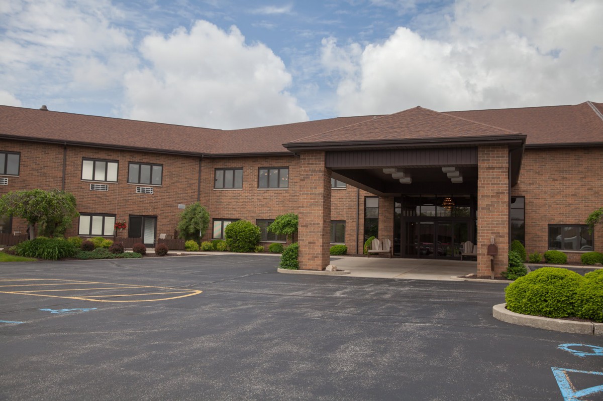 A two-story brick building with a parking lot and cloudy skies above.