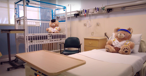 A pediatric hospital room featuring a crib for infants, a chair for parents, and a stuffed toy.