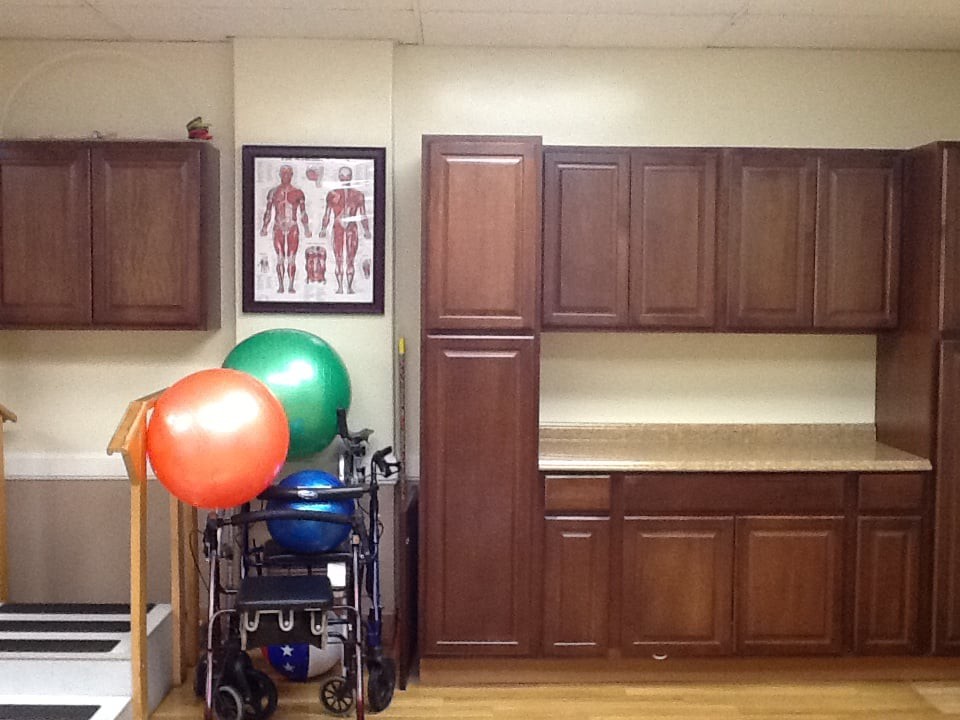A physical therapy room featuring exercise balls, a medical anatomy chart, and storage cabinets.