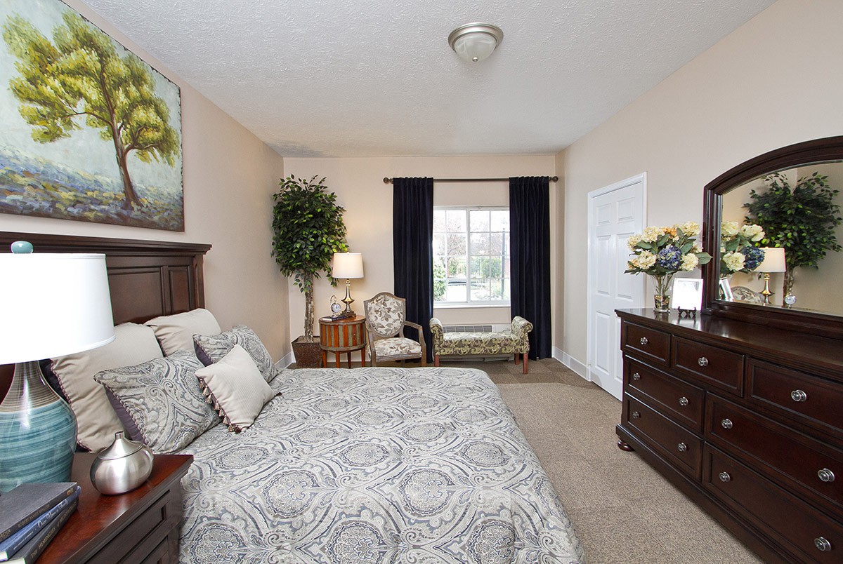 A cozy bedroom with a large bed, dresser, and seating area by the window.