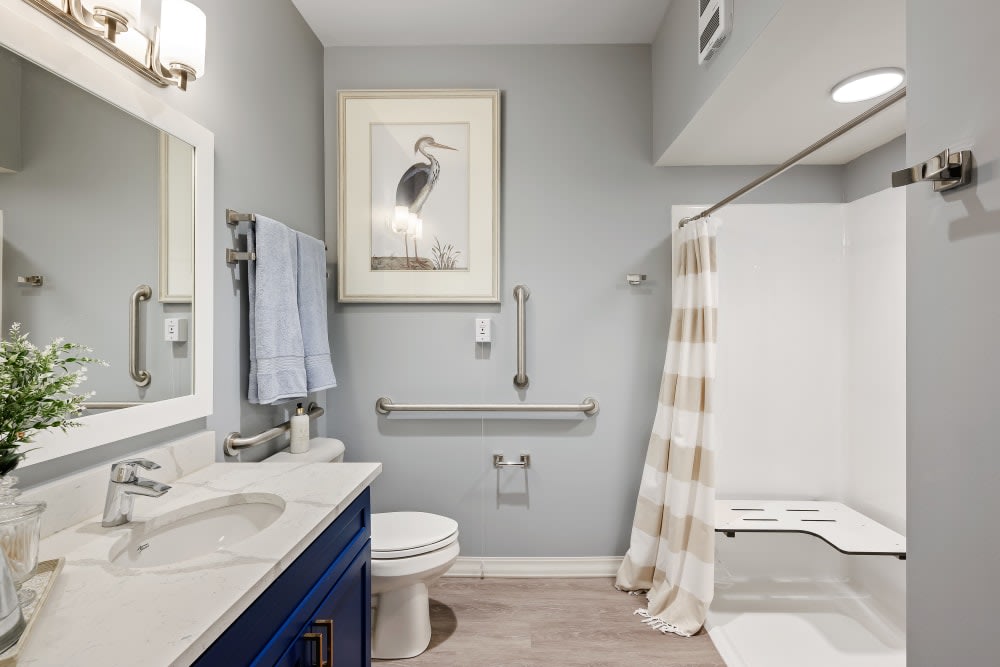 A modern bathroom with a blue vanity, large mirror, and neutral decor.