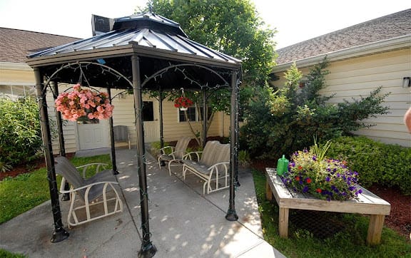 A charming garden patio with a gazebo and outdoor seating surrounded by lush greenery and flowers.