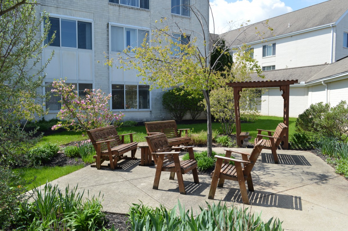 A peaceful garden with wooden seating and a pergola next to an apartment building.