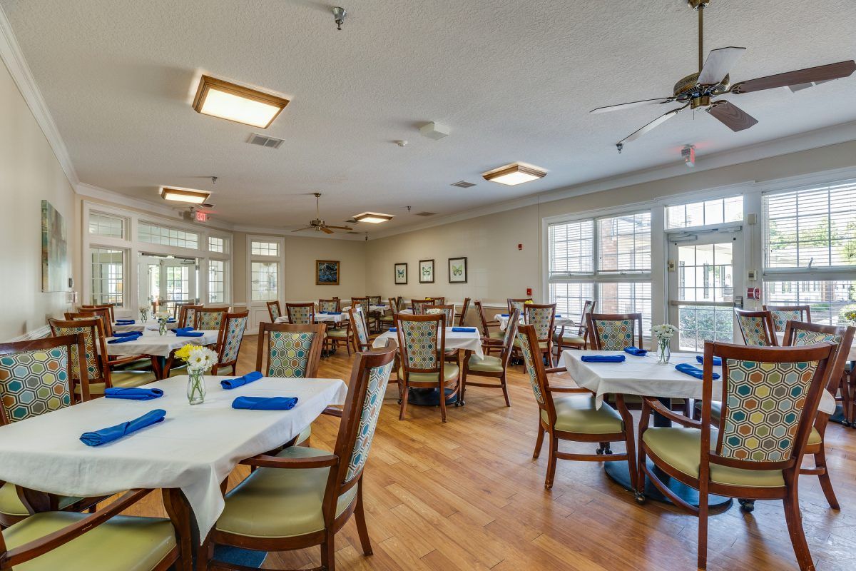 A spacious dining room with neatly arranged tables and chairs, featuring large windows and wooden flooring.