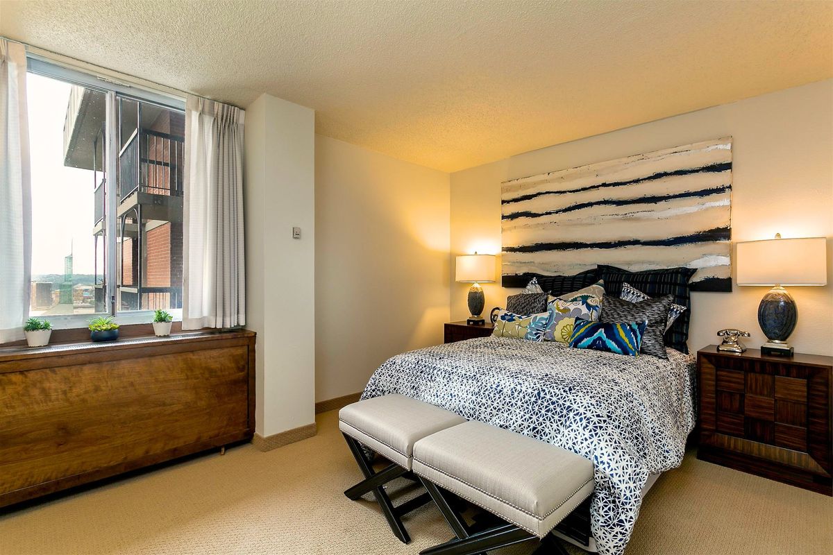 A modern bedroom with stylish decor featuring a large bed, abstract artwork above the headboard, and a window letting in natural light.
