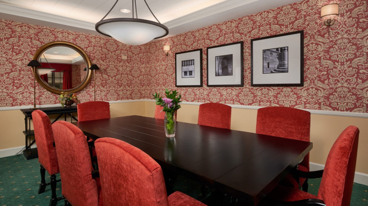 A stylish dining room with red upholstered chairs and a dark wooden table, complemented by patterned wallpaper and framed photos on the wall.
