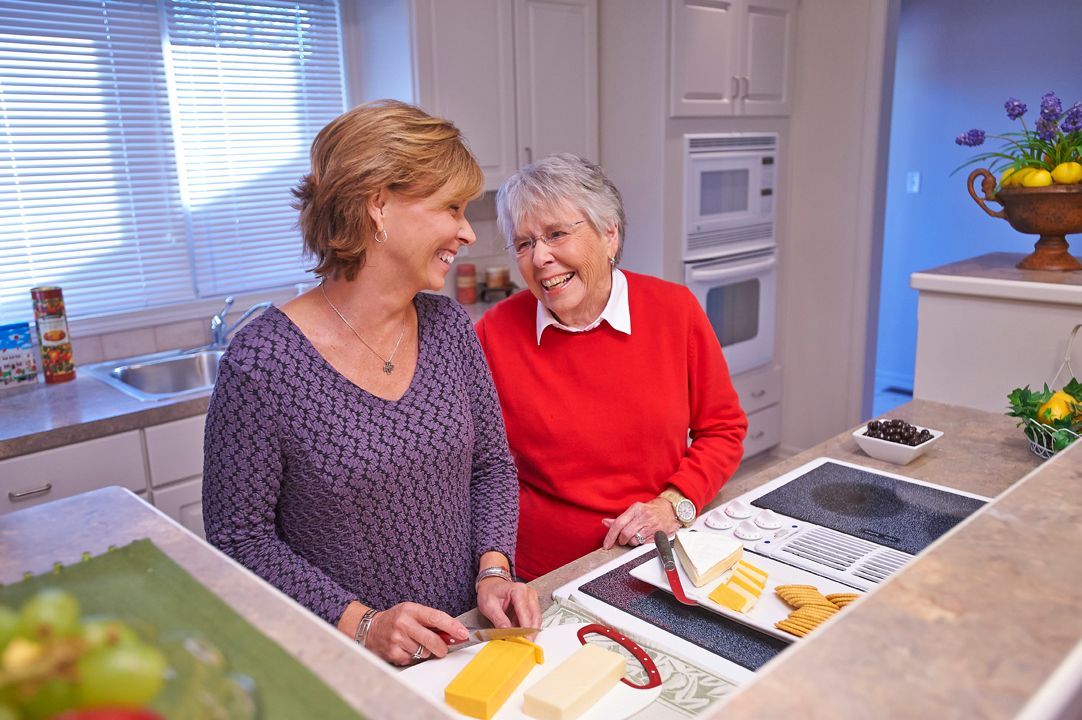 Two women smiling and preparing food together in a kitchen.