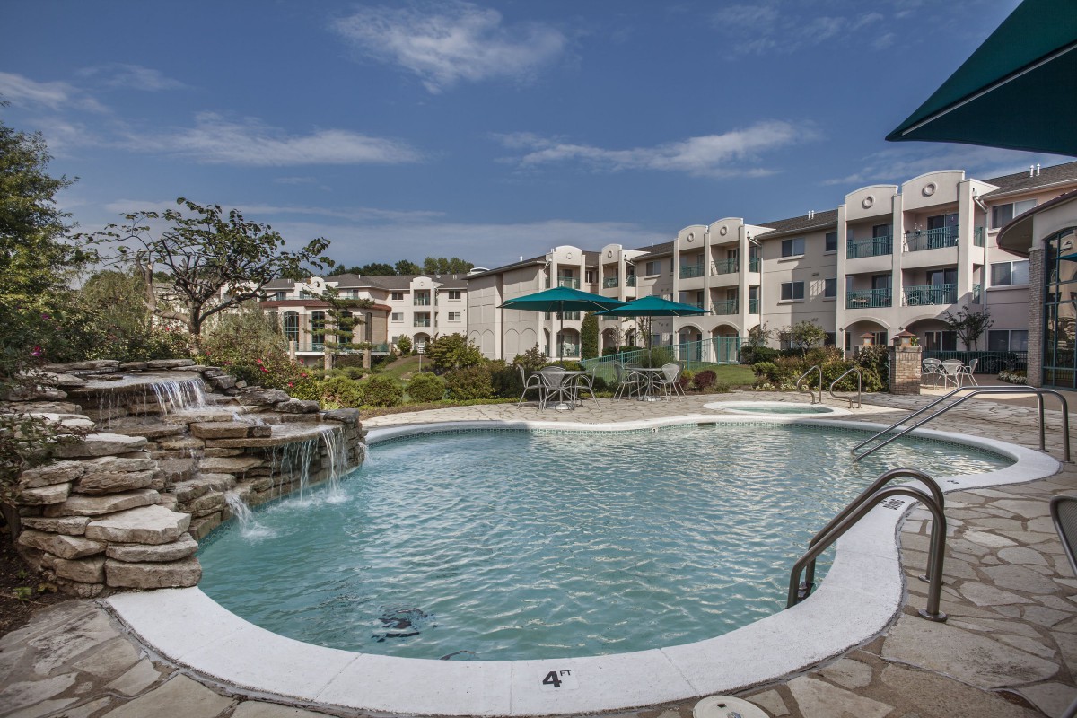 A scenic view of a swimming pool in a residential complex with apartment buildings in the background.