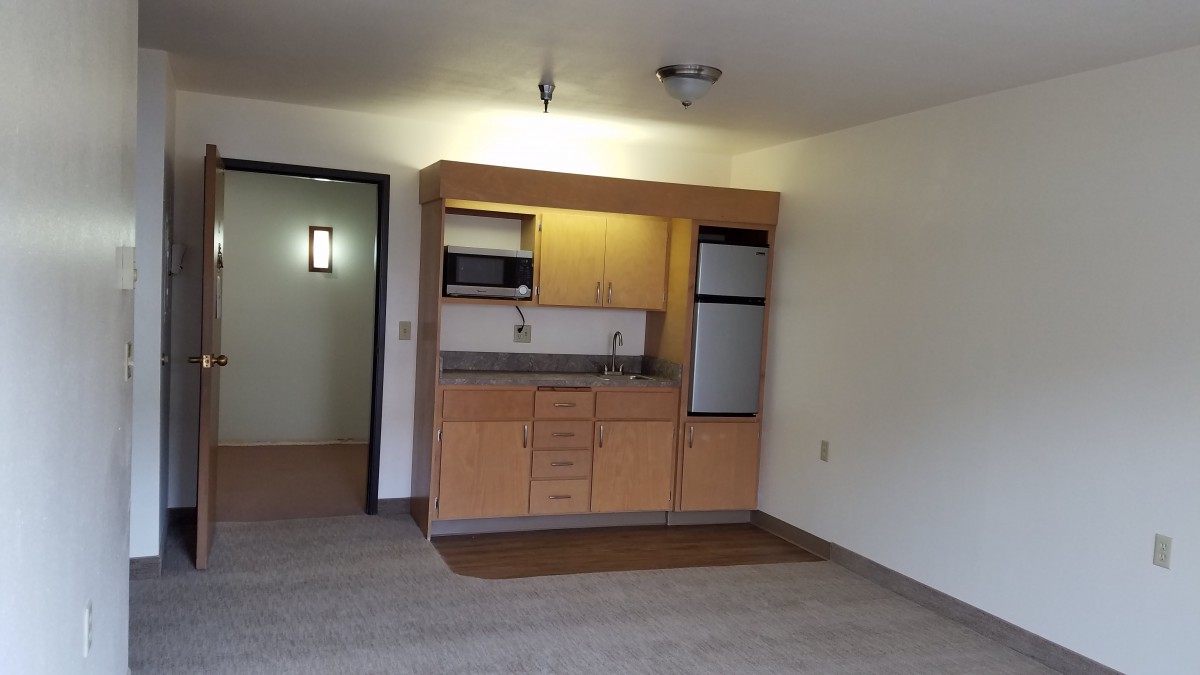 A compact kitchenette in an apartment with wooden cabinets and a small fridge.