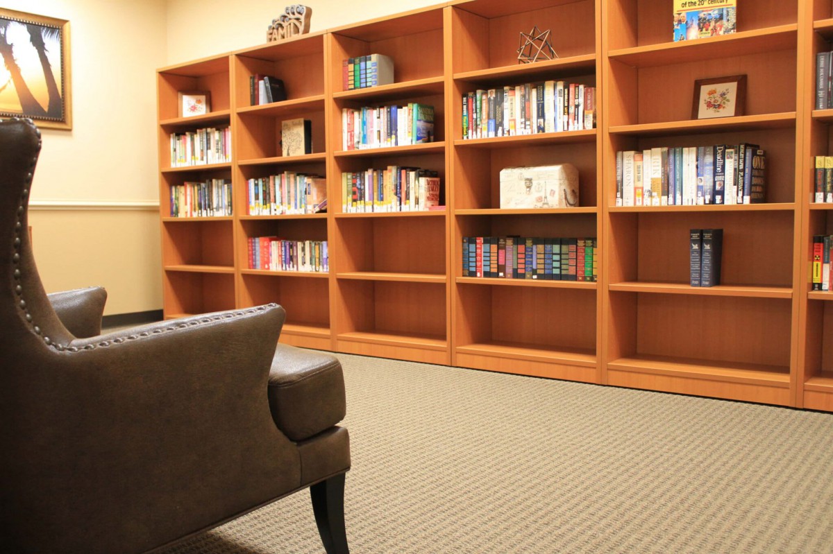 A cozy library corner with a large wooden bookshelf filled with books, and an armchair in the foreground.