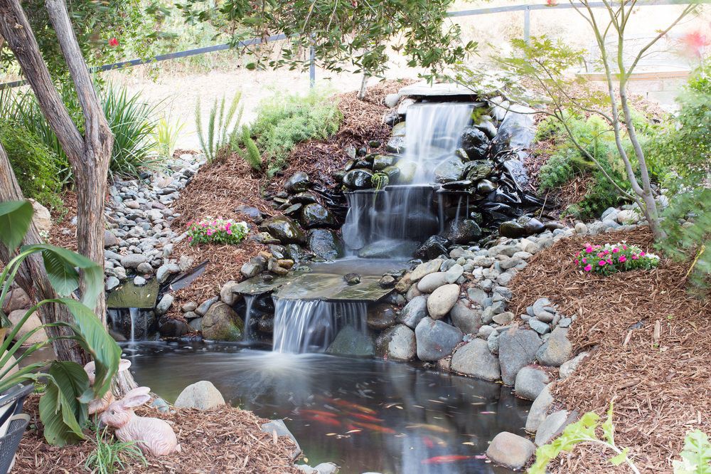 A serene garden pond with a cascading waterfall surrounded by rocks and greenery.