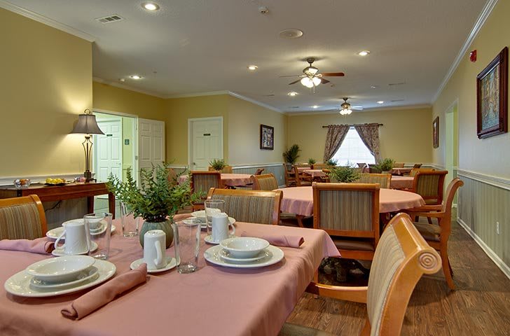 A cozy dining room with neatly arranged tables and chairs, featuring elegant table settings and warm lighting.