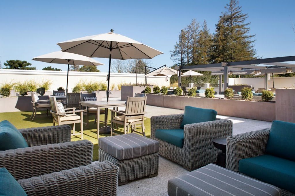 A spacious outdoor patio with wicker furniture, including chairs, tables, and umbrellas under a clear blue sky.