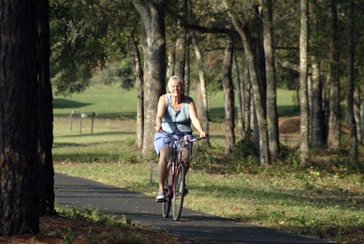 A woman enjoying a leisurely ride on her bicycle along a scenic path surrounded by trees.