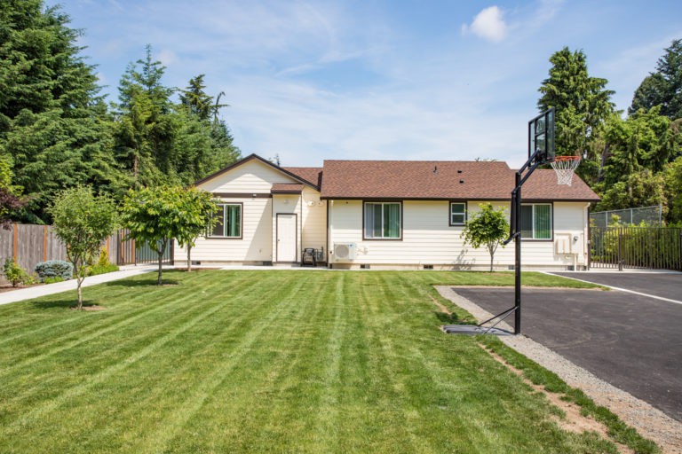 A suburban single-story house with a well-maintained lawn and a basketball hoop in the driveway.