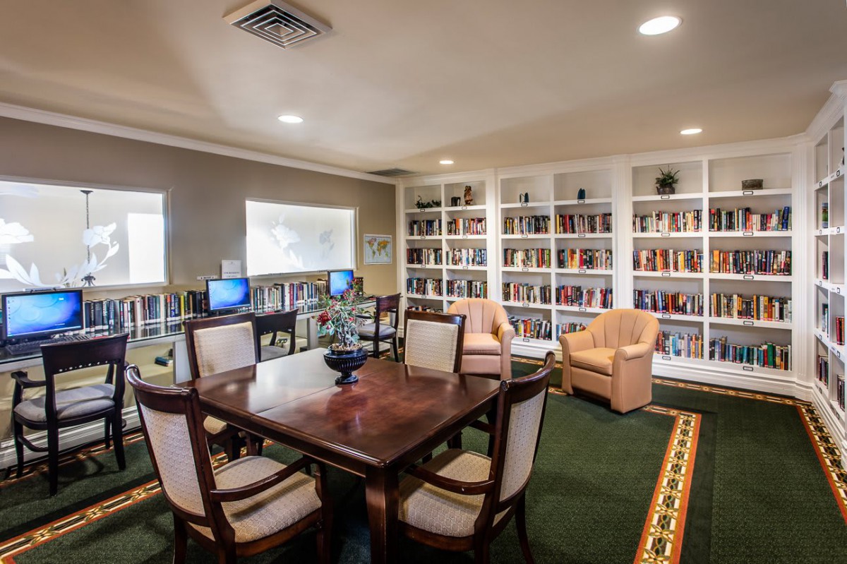 A cozy library room with bookshelves, a central table, chairs, and computers for study.
