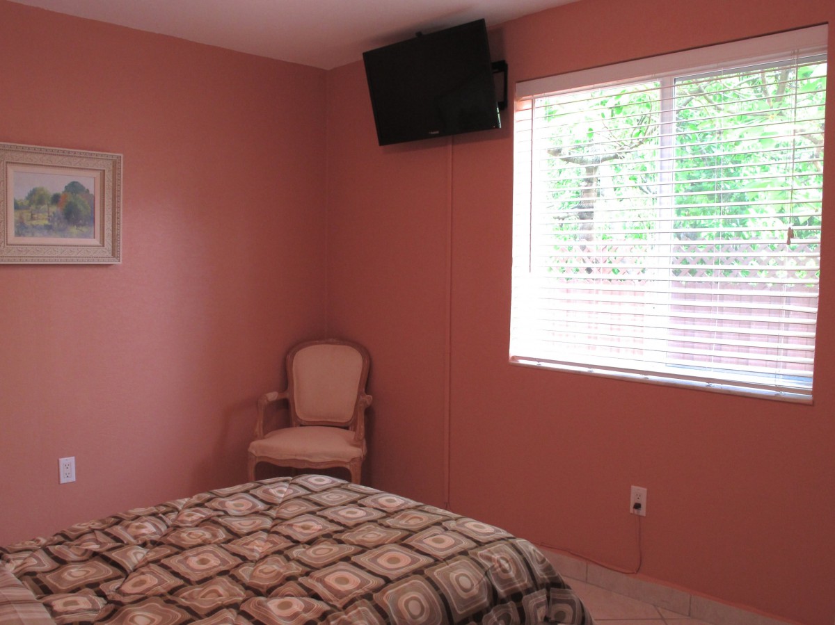 A cozy bedroom with pink walls, a chair, and a wall-mounted television.