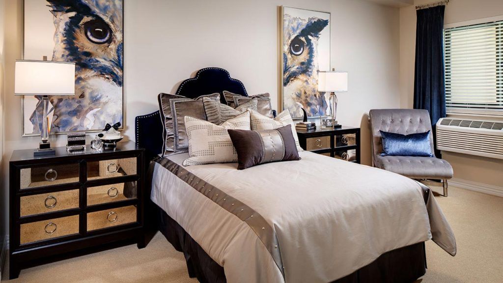 A stylishly decorated bedroom with a bed adorned with multiple pillows, bedside tables, and artwork hanging on the walls.